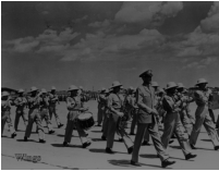 Jimmy Stewart, in role as Glenn Miller, marching with the band along one of Lowry AFB’s taxiways.  [Wings]