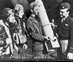 Two students (left) are briefed for a night mission while a sergeant carries a flash bomb for taking photos in the dark.  (Wings)